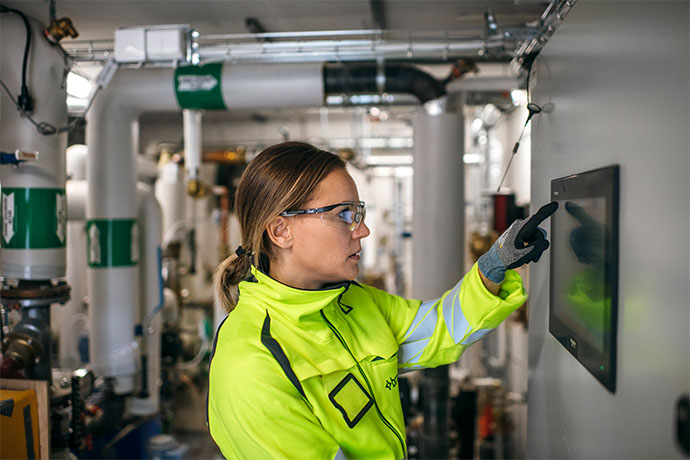 Bilden visar en tekniker vid en styrpanel i en industriell miljö