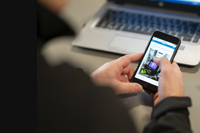 En bild på en mobiltelefon i handen vid en dator